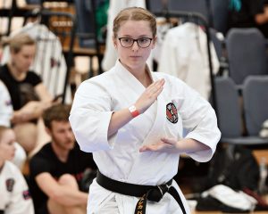 a young blonde girl with glasses performs a karate move wearing a gkr karate gi